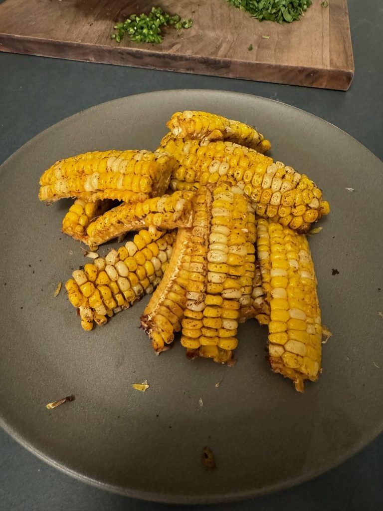 Air-fried seasoned corn ribs piled on a plate before topping, with chopped cilantro on a board behind