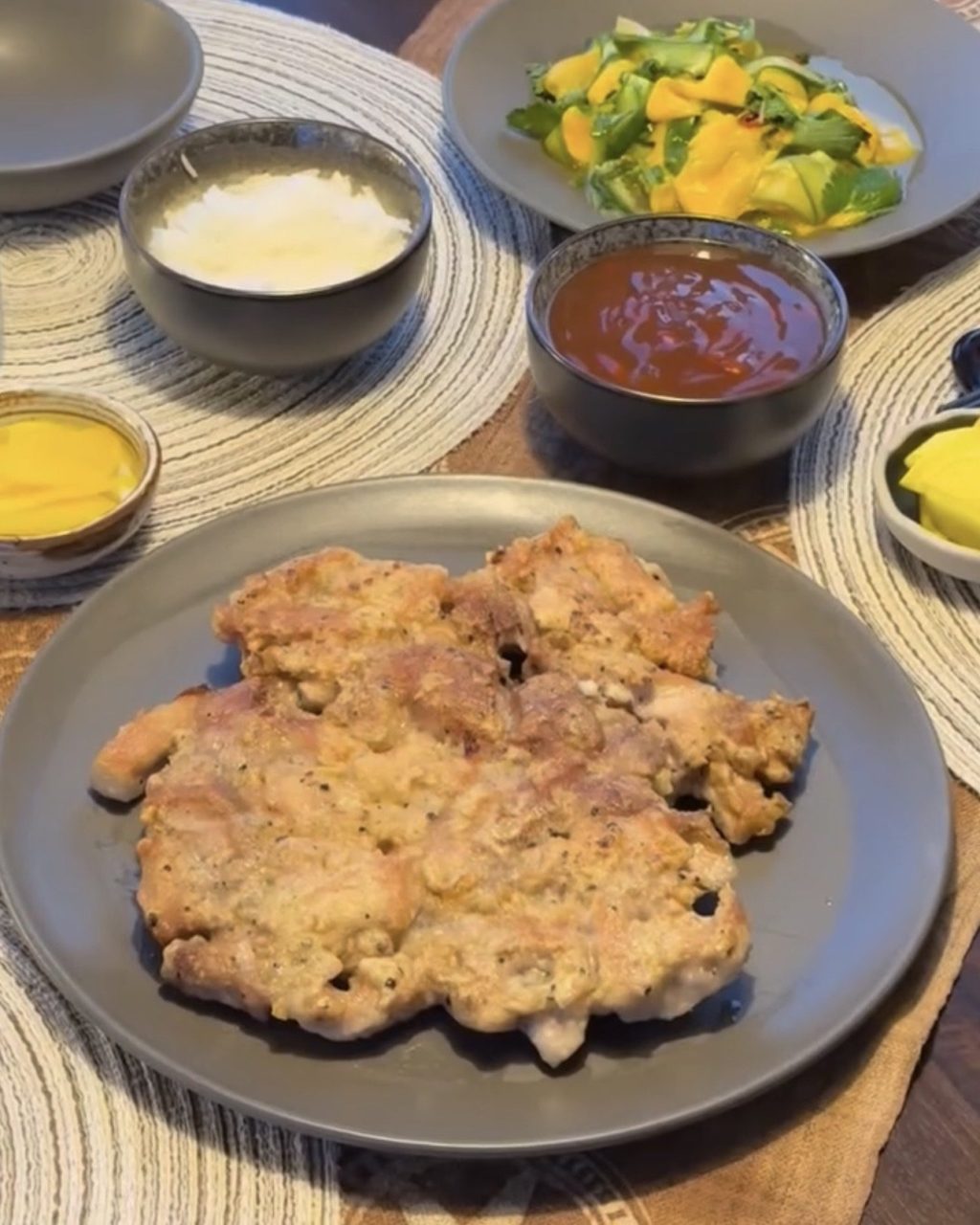 Golden pan-fried battered pork on a gray plate, with a bowl of sweet and sour sauce and side dishes on the table