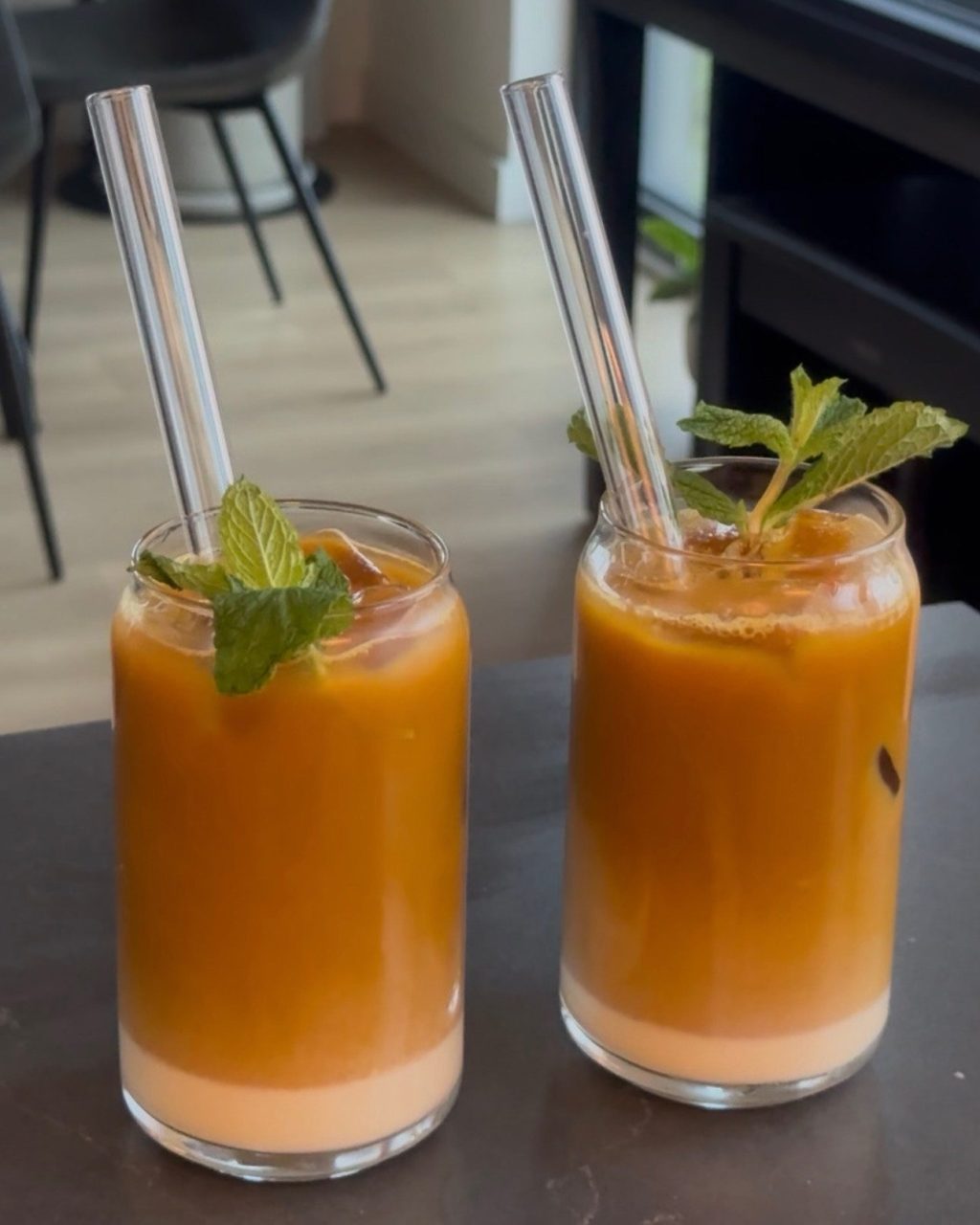 Two glasses of Thai iced tea with glass straws and mint sprigs, the orange tea layered over cream