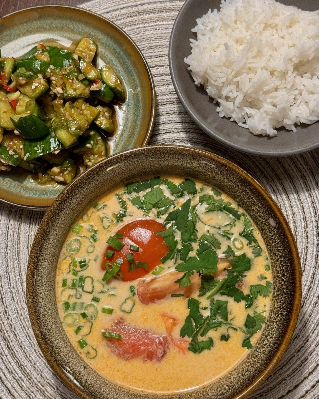 Bowl of creamy coconut tom kha soup topped with cilantro and green onion, with rice and a cucumber salad on the side