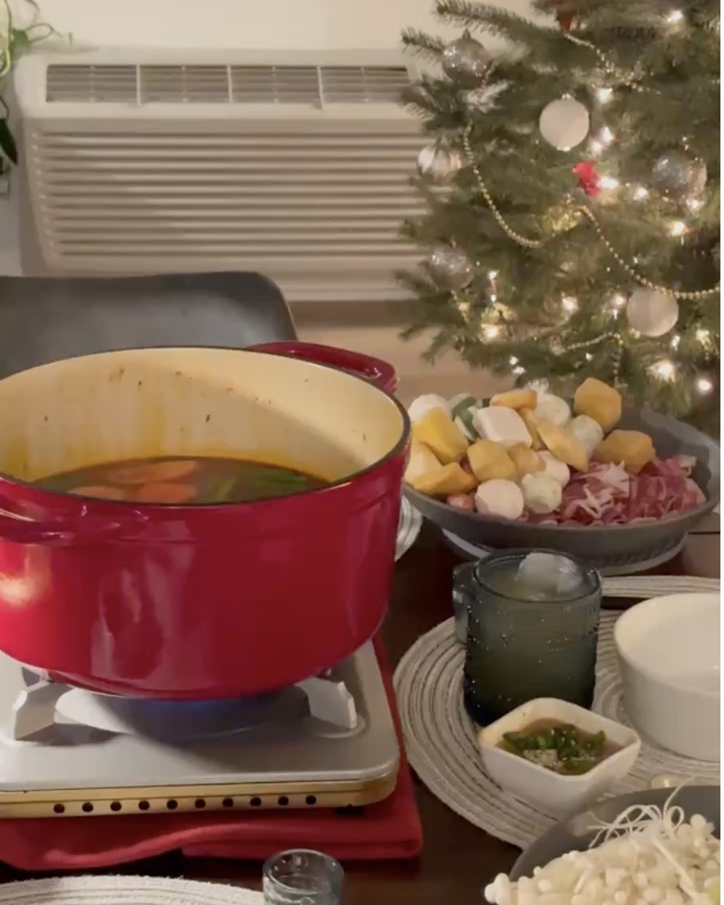 Red pot of tomato hot pot broth on a tabletop burner, with plates of hot pot ingredients and dipping sauces around it