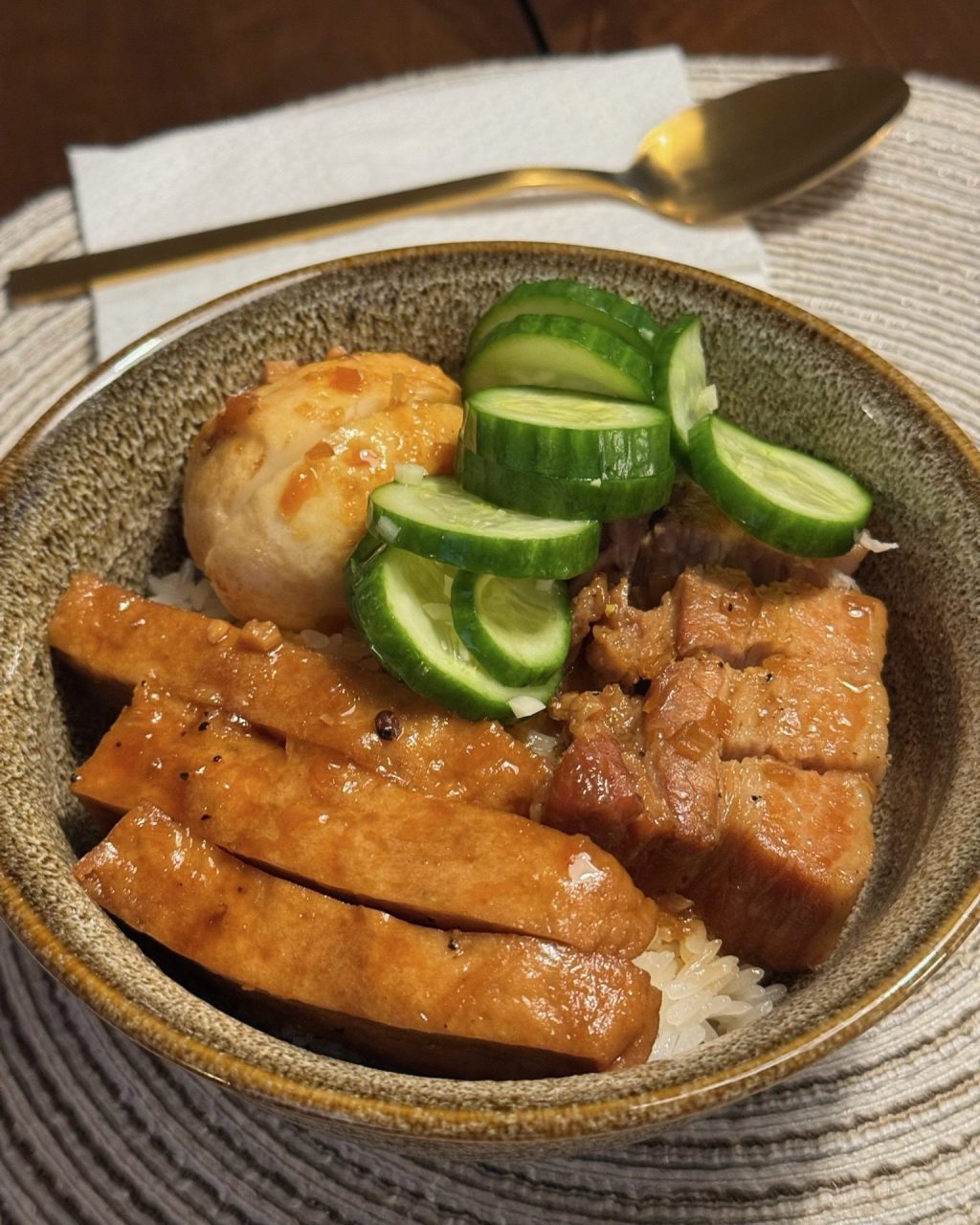 Bowl of sticky rice topped with braised pork belly, sliced chả, a fried egg and pickled cucumber
