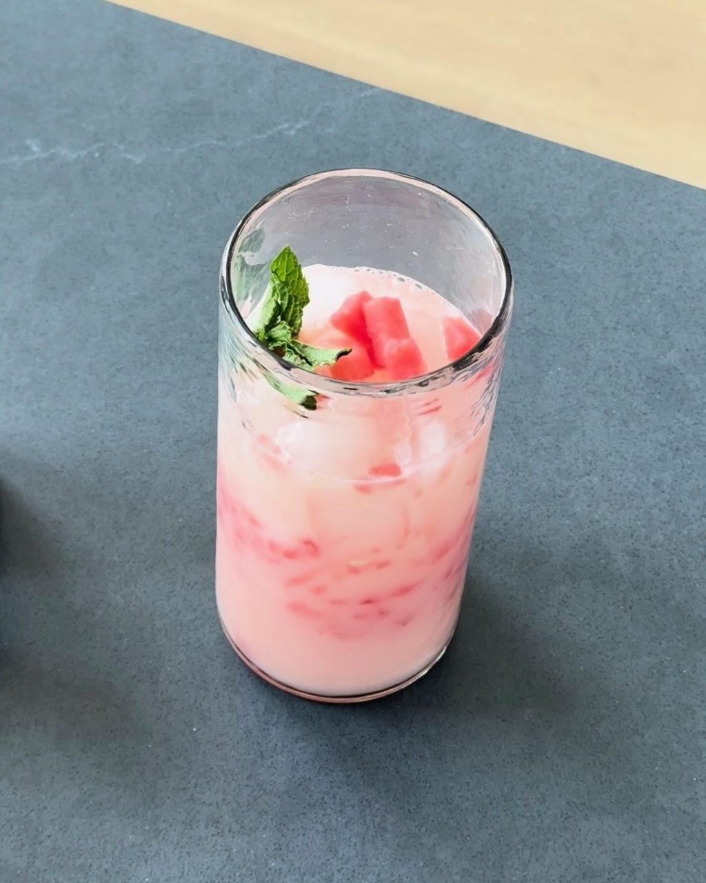 A tall glass of pink Yakult watermelon refresher over ice, garnished with watermelon cubes and a mint sprig