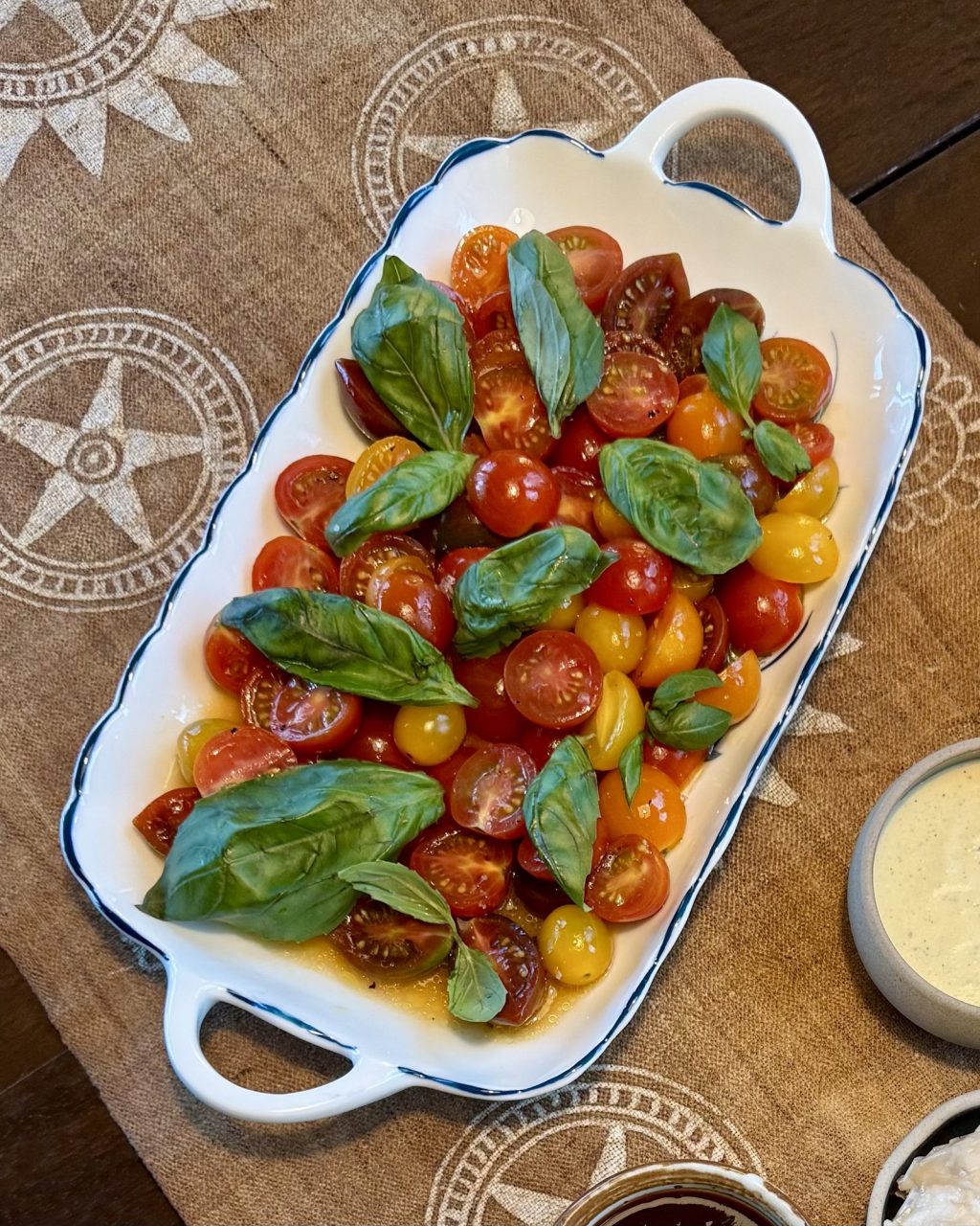 Red, orange and yellow cherry tomatoes tossed with yuzu dressing and fresh basil leaves on a white platter